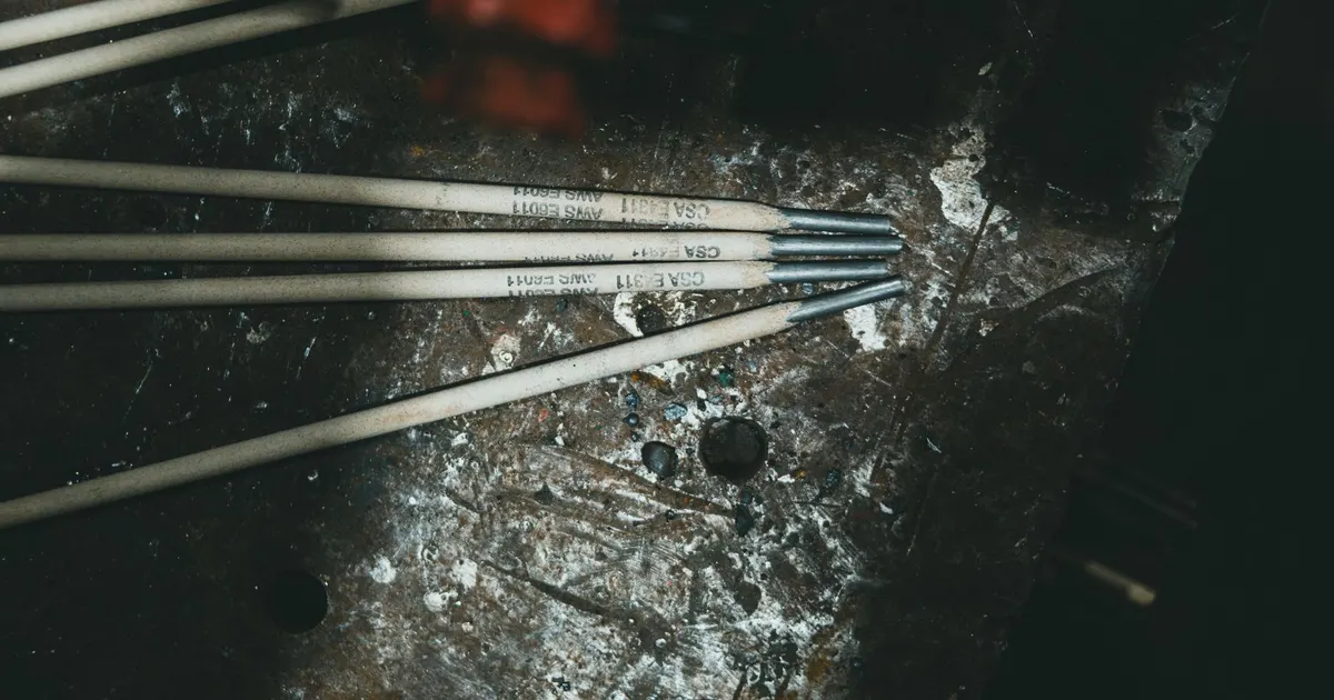 Four stick welding electrodes lying on a scarred steel workbench, each marked with an AWS classification, an example for filler metal selection