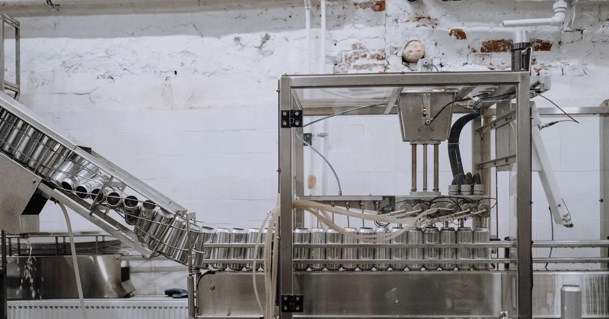 Can filling machine with a metal frame and conveyor in a small production hall, an example of food and packaging machinery weldments
