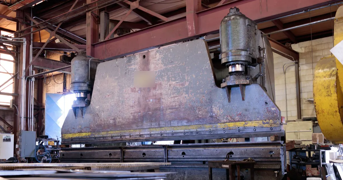 Large press brake with a plate side frame and two vertical cylinders standing in a fabrication workshop, an example of a press frame weldment